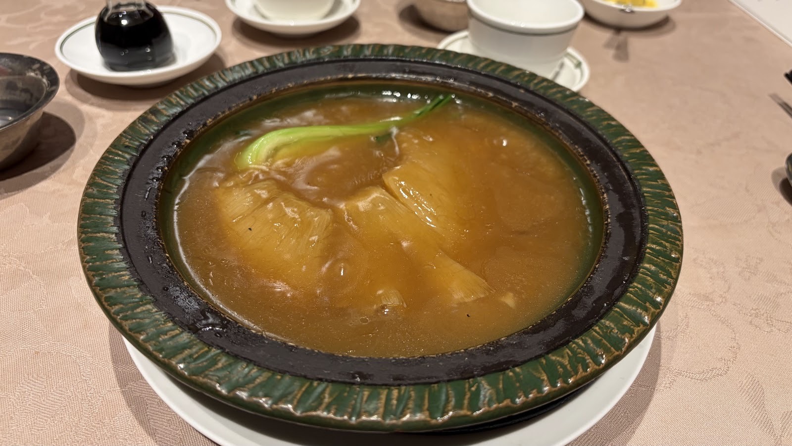 白い皿に載せた緑釉の壺。中に濃い茶色のとろみのあるソースで煮込んだふかひれと青菜。