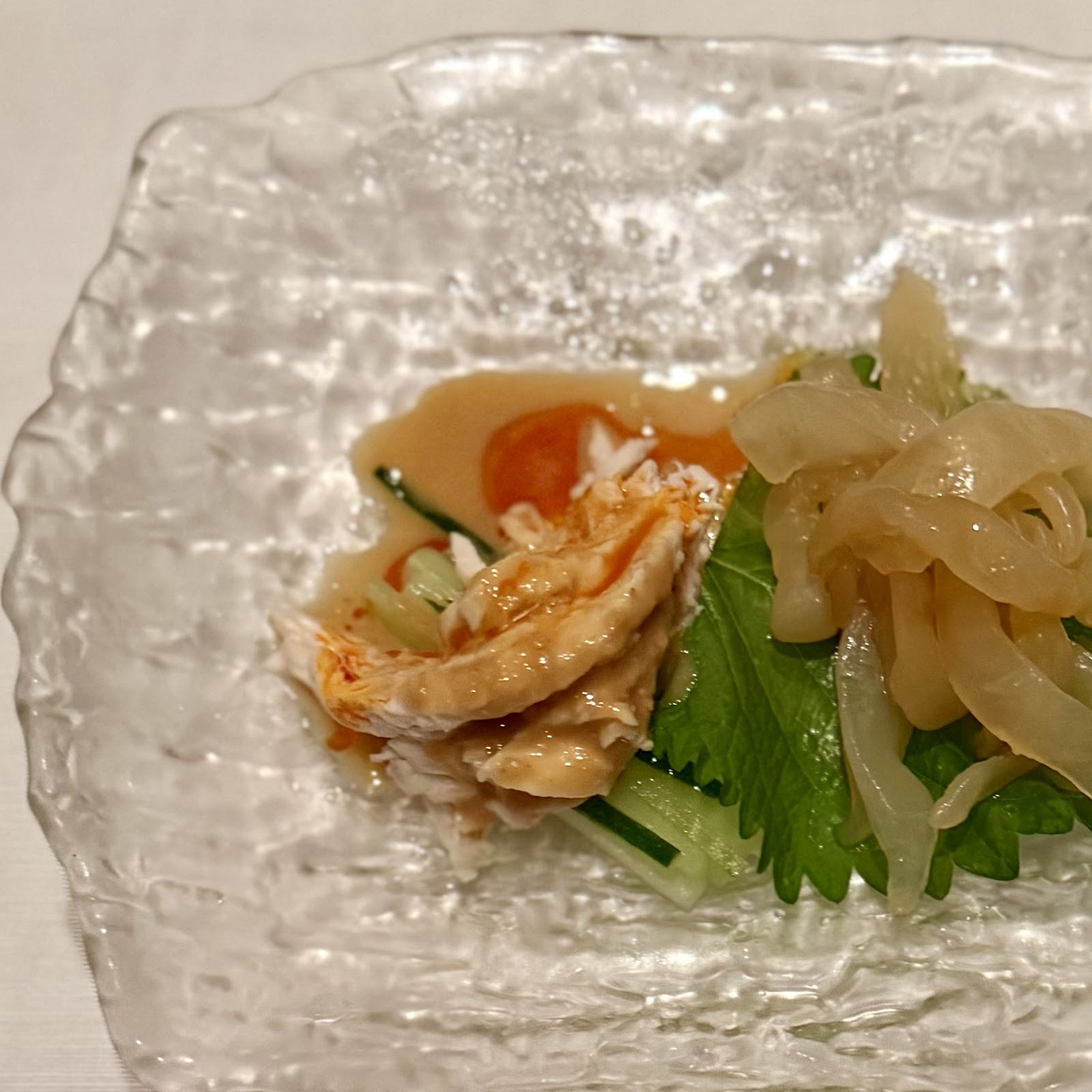 凹凸のあるガラスの皿に盛った前菜。くらげ、鶏肉のスライス、ミニトマト、きゅうり、葉もの。